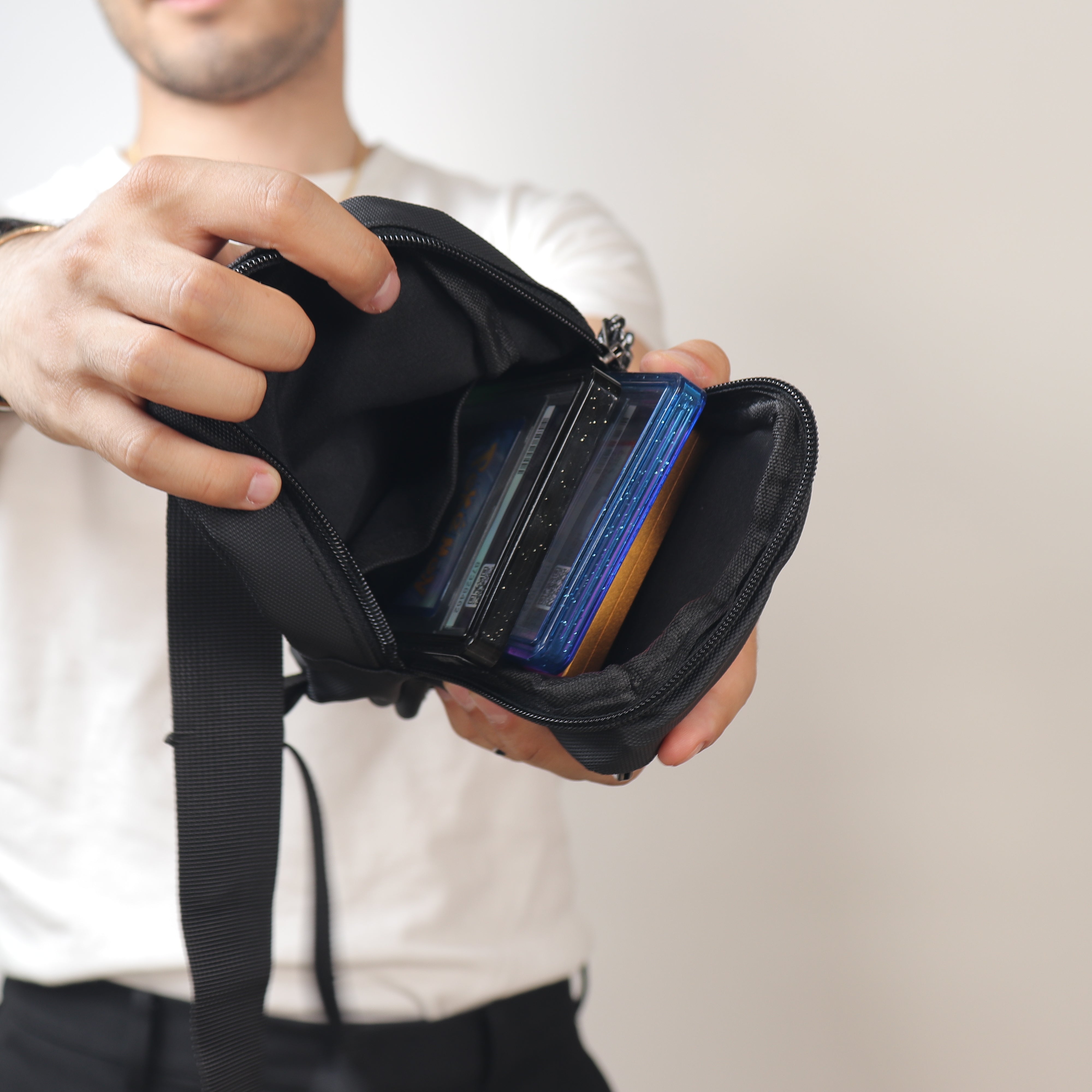 A close-up of a person holding open a black zippered card holder or wallet pouch, showing several cards inside, against a plain light background.